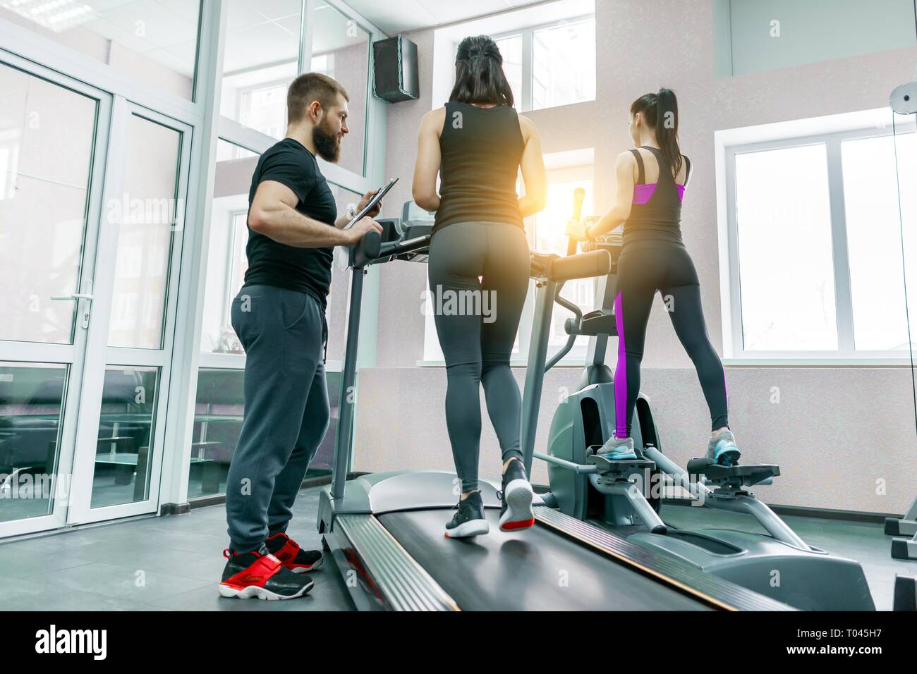 Young athletic women on treadmill, personal instructor coaching and helping client woman. Fitness, sport, training, people concept Stock Photo