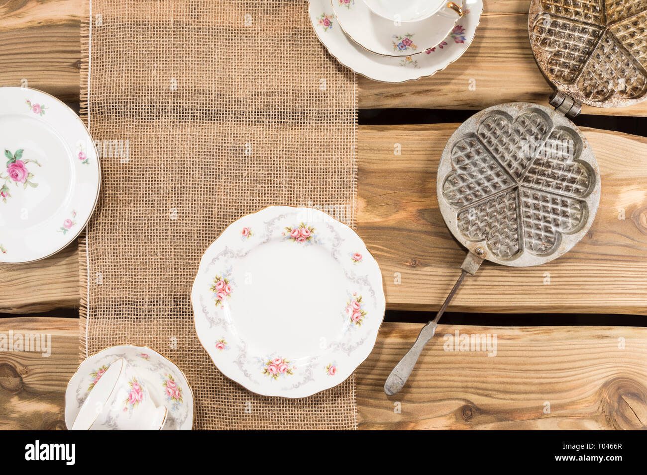 Old romantic porcelain and ancient waffle iron arranged on rustic wood planks. Shot from above, flat lay. Stock Photo