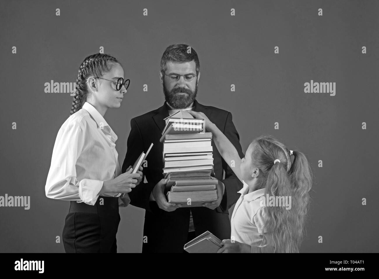 Teacher man and girls hold book pile at school. School time of sisters and father in library. Education in knowledge day. Literature lesson and Stock Photo
