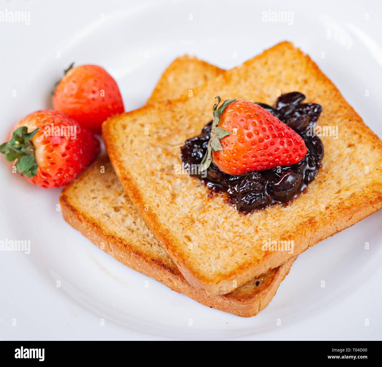 Table top close up of bread toast with the toppings of cranberry jam and Strawberry in white plate. Stock Photo