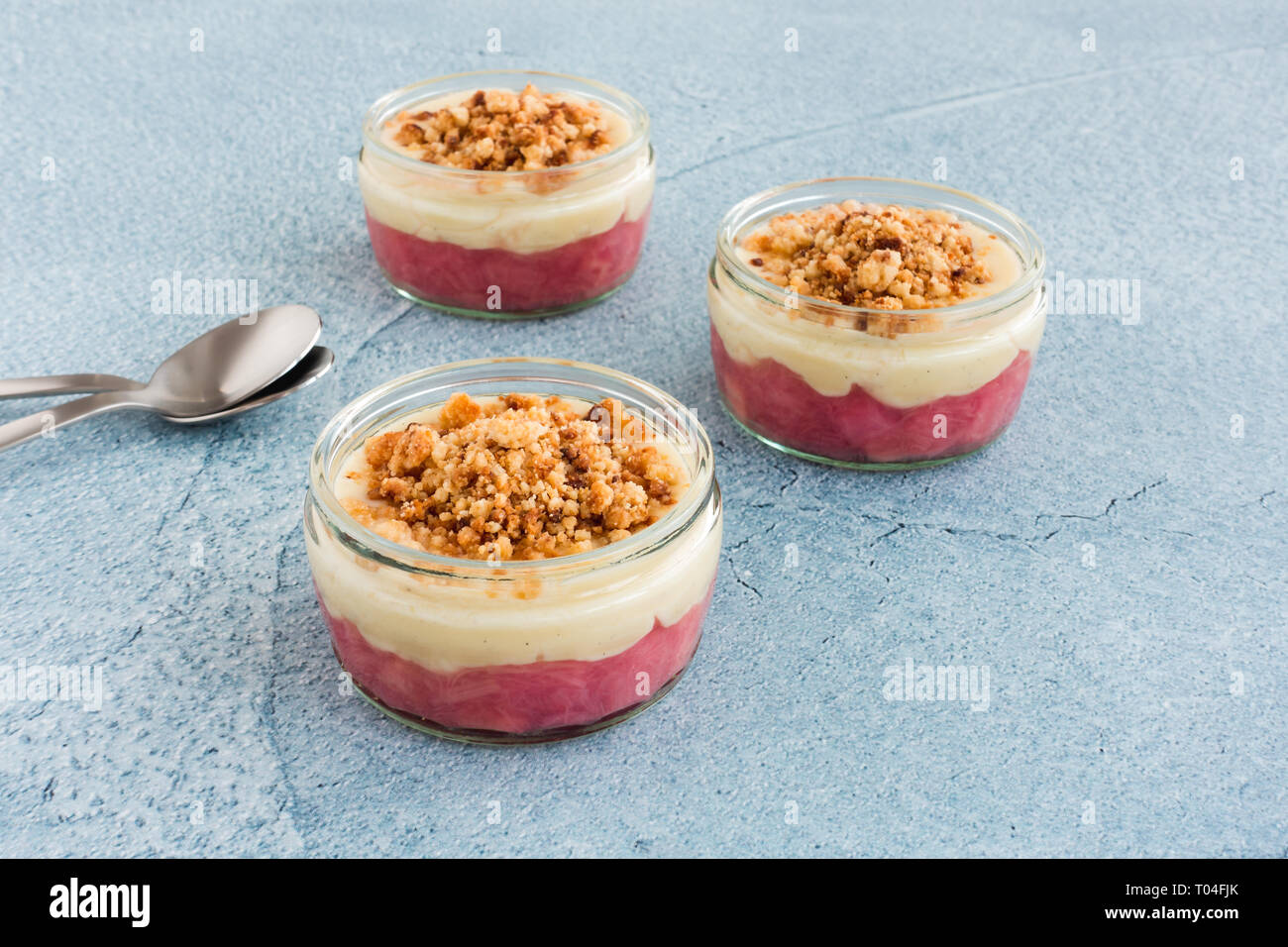 Closeup of homemade rhubarb and madagascan vanilla custard dessert with crumbs in glass regards on blue cement background with copy space. Stock Photo