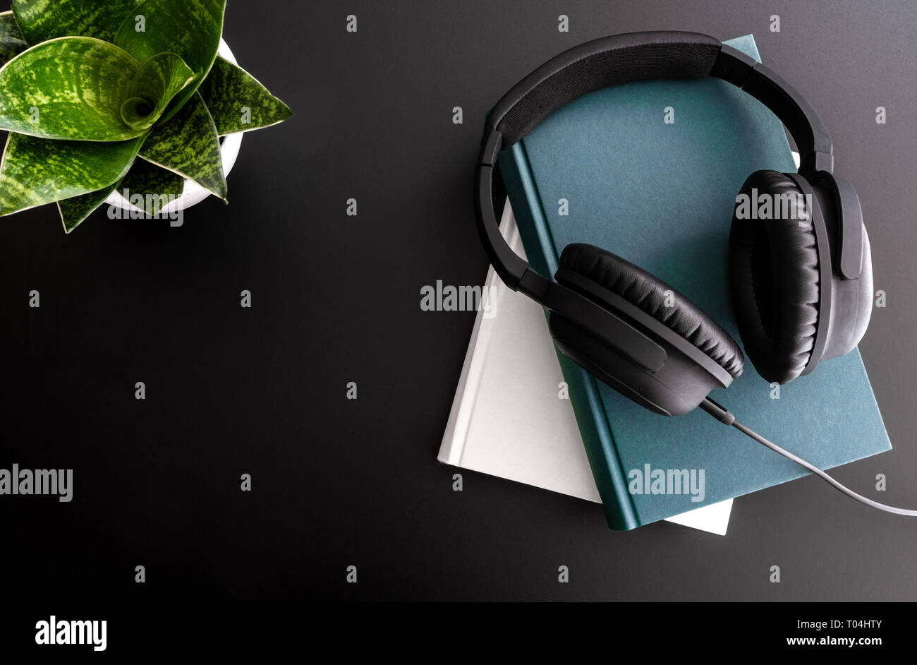 audiobook concept with overhead shot of headphones on stack of books on black background Stock Photo