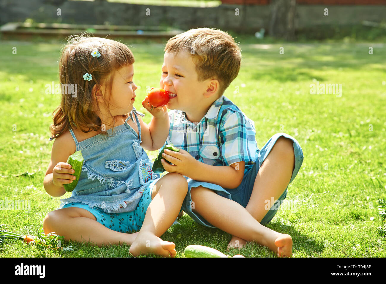 children outdoors in the summer. brother and sister eating vegetables Stock Photo