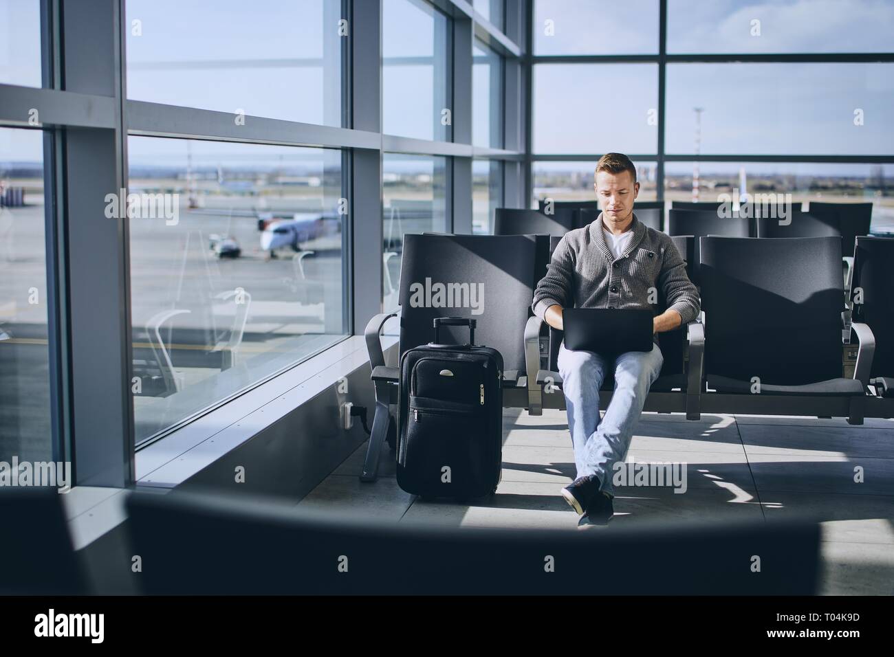 Traveler using laptop in airport terminal. Young man waiting for airplane. Stock Photo