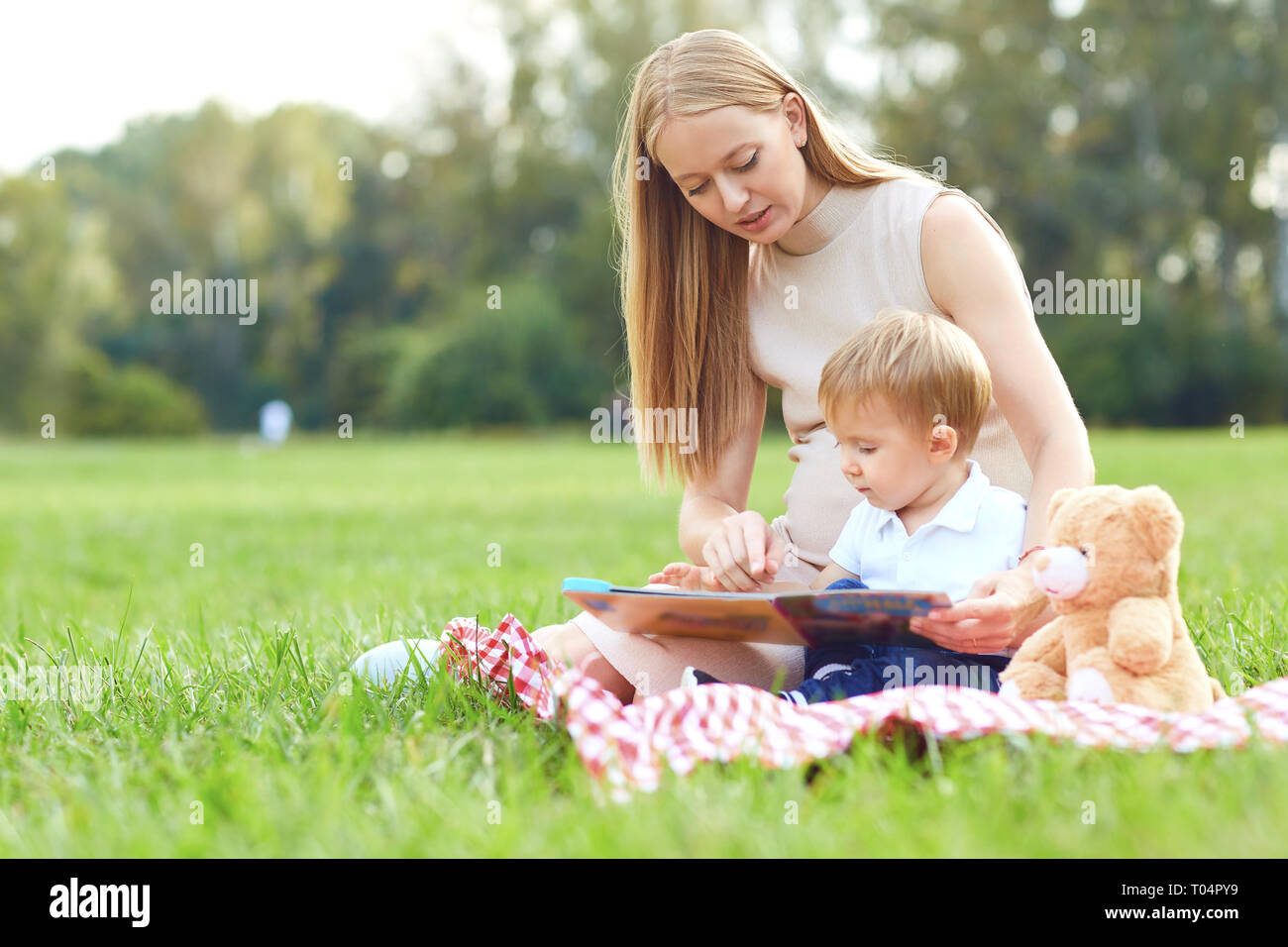 Mother with child reads on the grass in the park.  Stock Photo