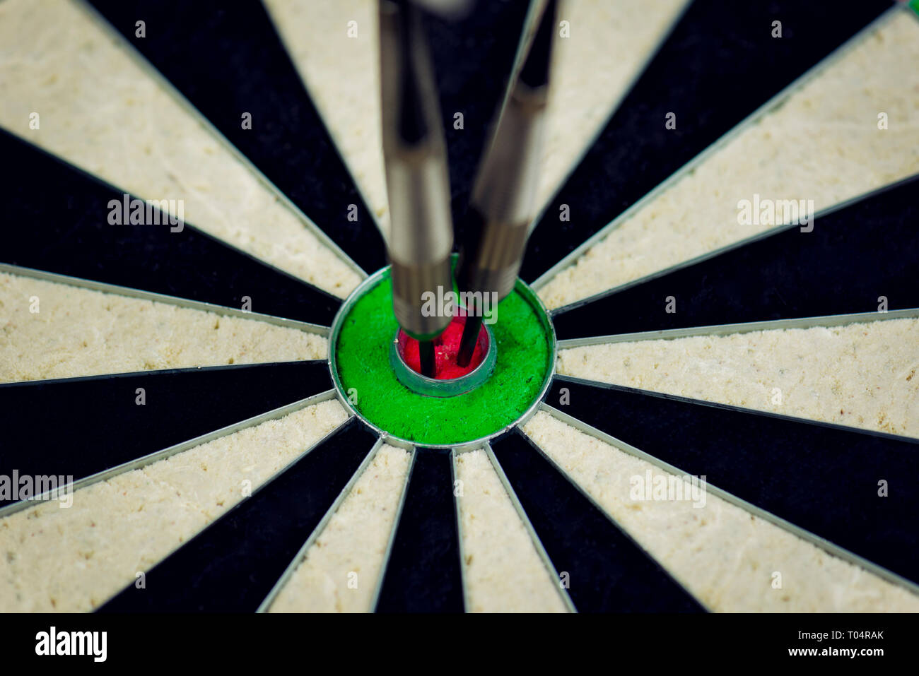 three darts thrown at the bulls eye of a dartboard Stock Photo