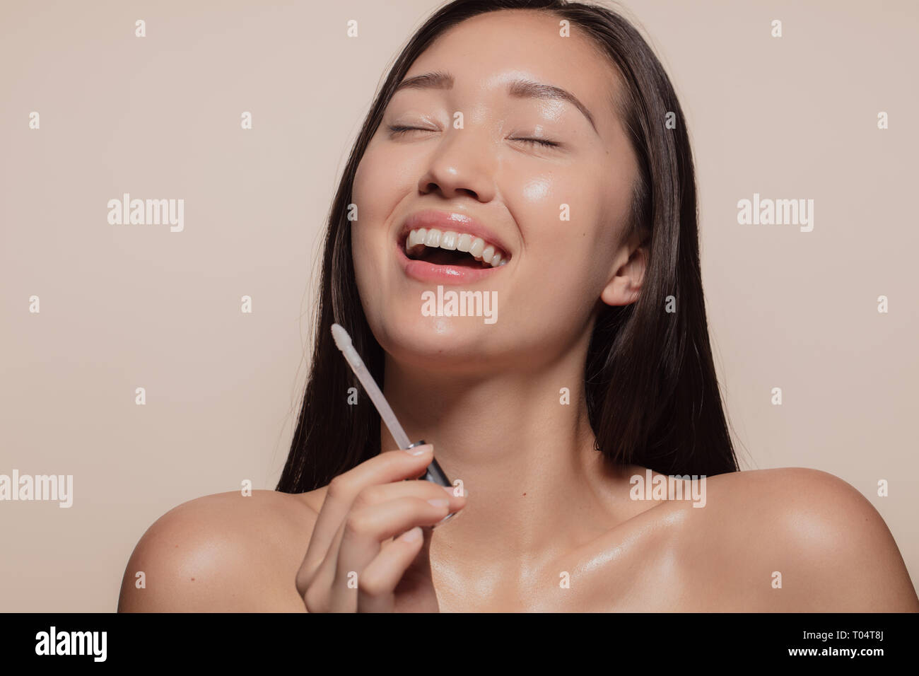 Young woman smiling with her eyes closed while doing makeup. Korean female model enjoying doing make up. Stock Photo