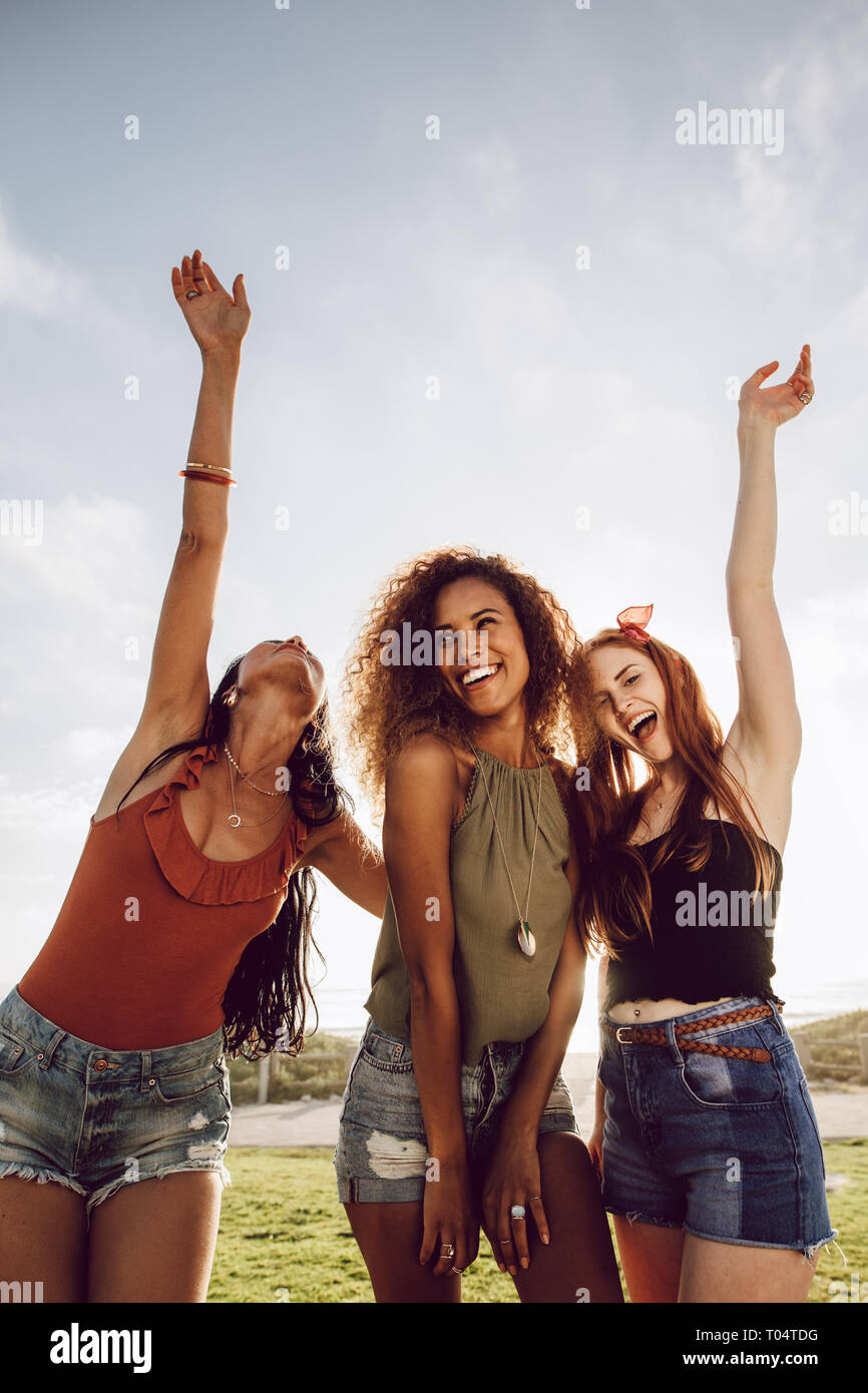 Beautiful young women standing outdoors laughing with their hand raised. Carefree girls enjoying themselves on summer holiday. Stock Photo