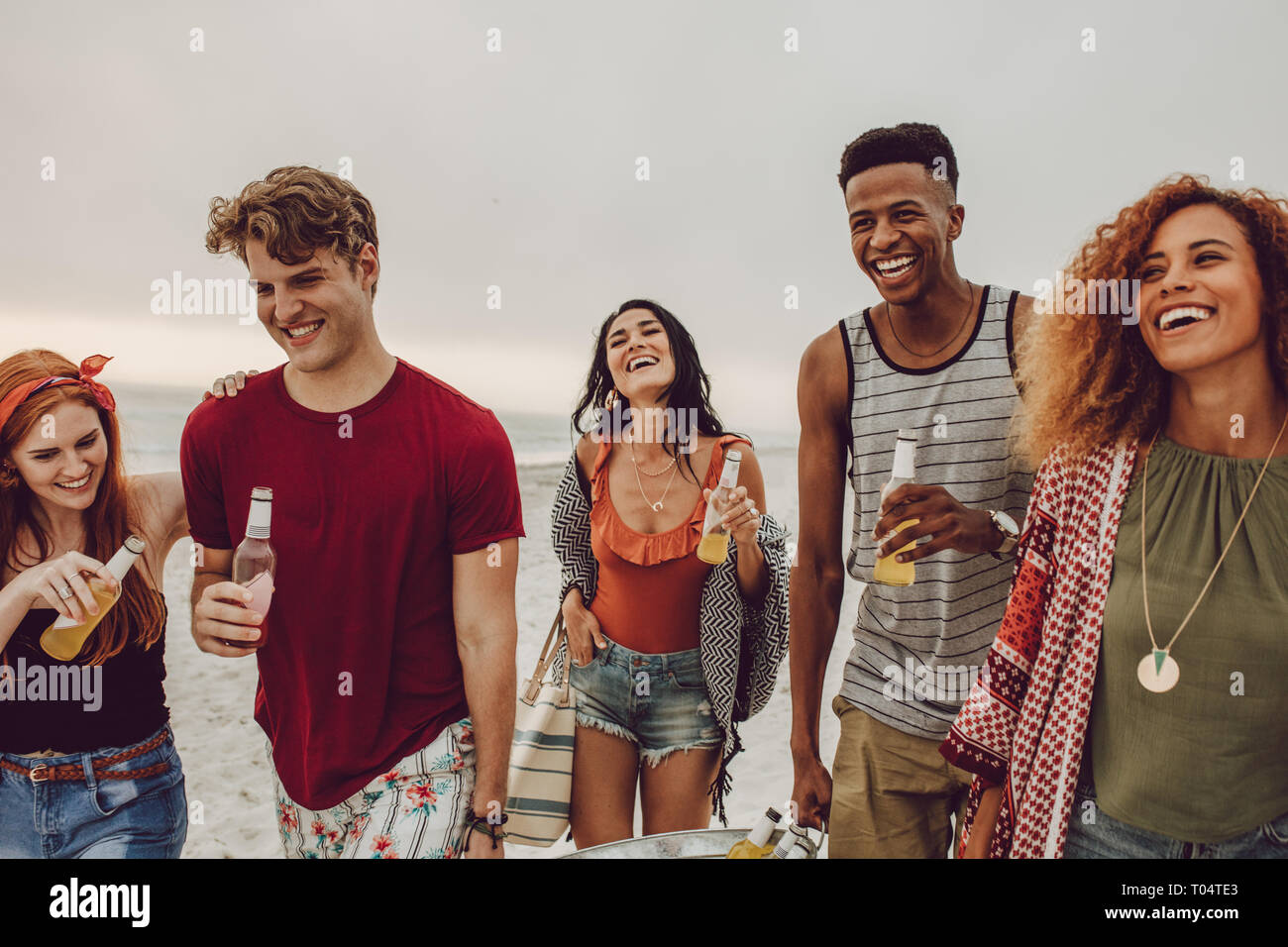 Group of people carrying beverage tub for party on beach. Diverse group of young people walking outdoors and having drinks. Stock Photo