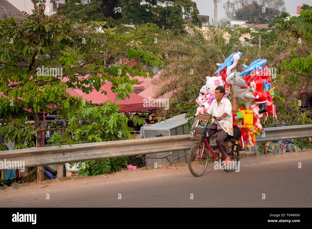 Elderly man transports his inflatable children toys via bicycle, Laos. Stock Photo