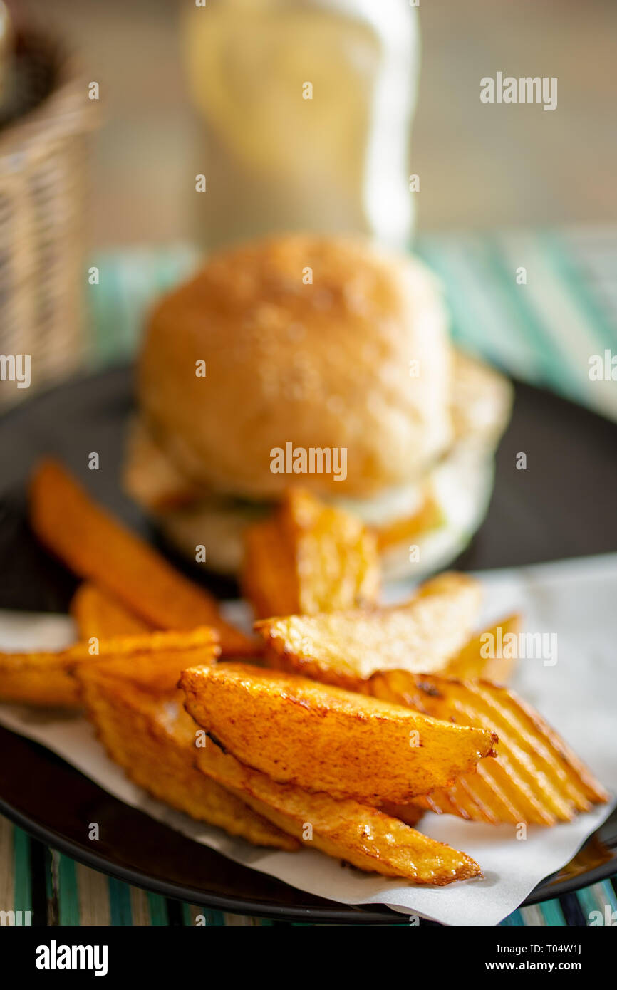 Plate of tasty hand cut fried to perfection chips fries with beef burger in bread bun. Stock Photo