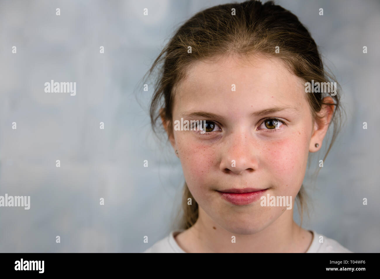 Authentic portrait of caucasian tween girl, very casual natural styling and neutral smile, on a light background with copy space Stock Photo