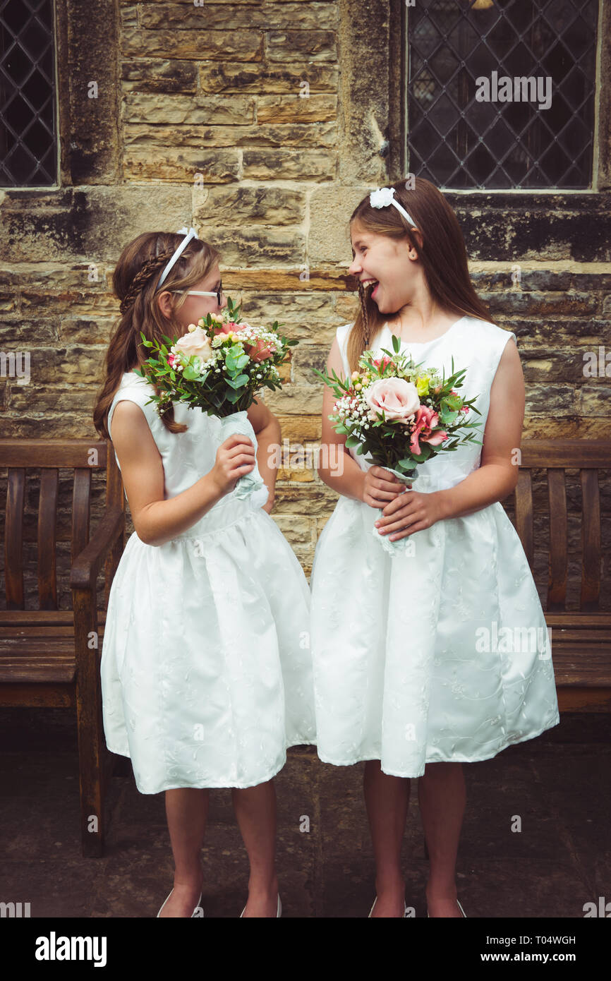 Beautiful young girl bridesmaids, child and tween or teen, holding rustic bouquets and wearing short white dresses in front of an old stone church Stock Photo