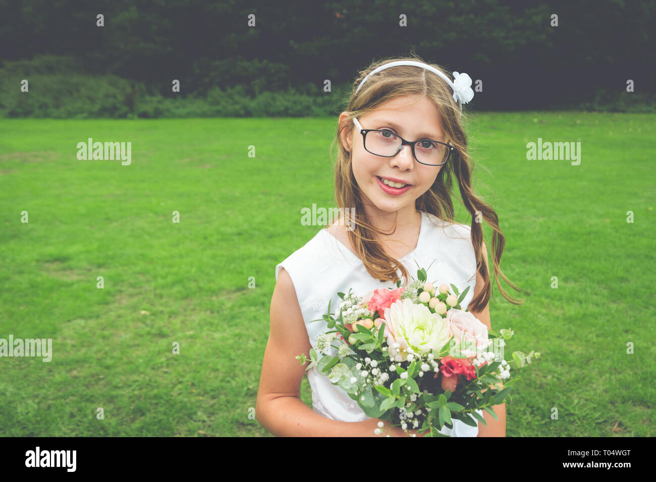 Sweet girl child bridesmaid in white dress and glasses with wildflower and greenery posy - natural shot Stock Photo