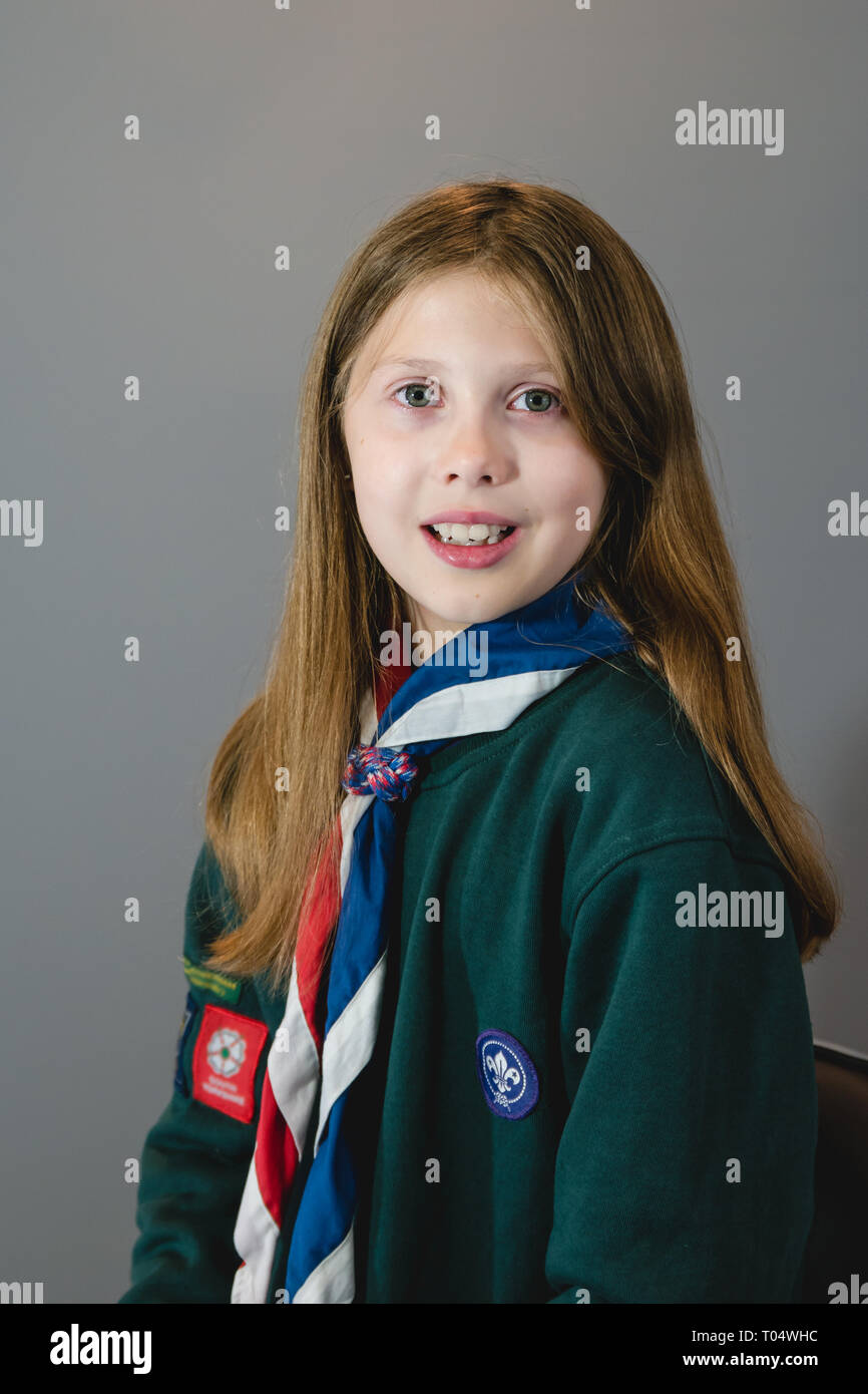 A portrait photo of a laughing British girl female cub scout in uniform with green sweatshirt, red, white and blue neckerchief and slider or woggle Stock Photo