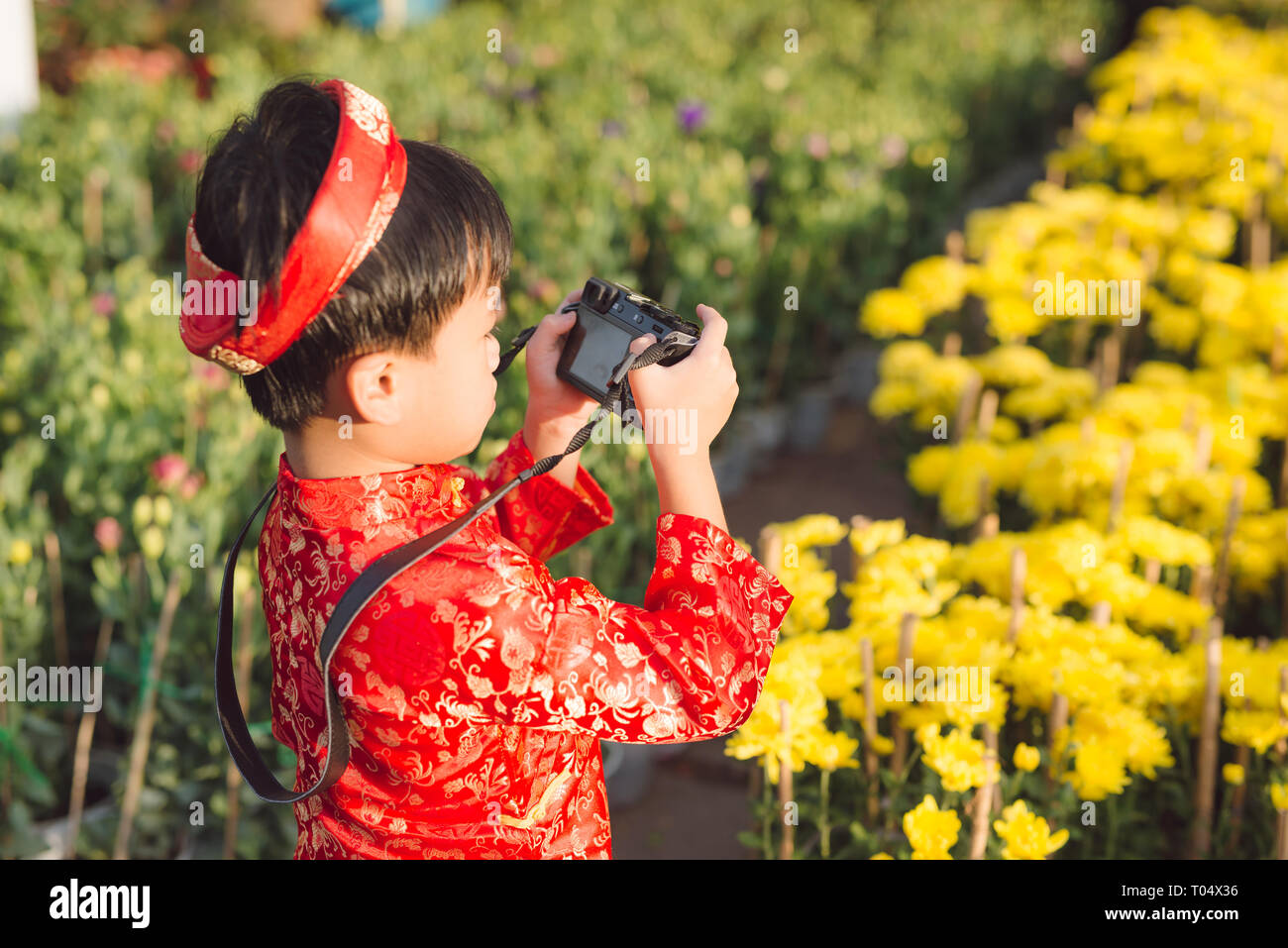 Child with digital compact camera outdoors. Cute little Vietnamese boy in ao dai dress. Tet holiday Stock Photo
