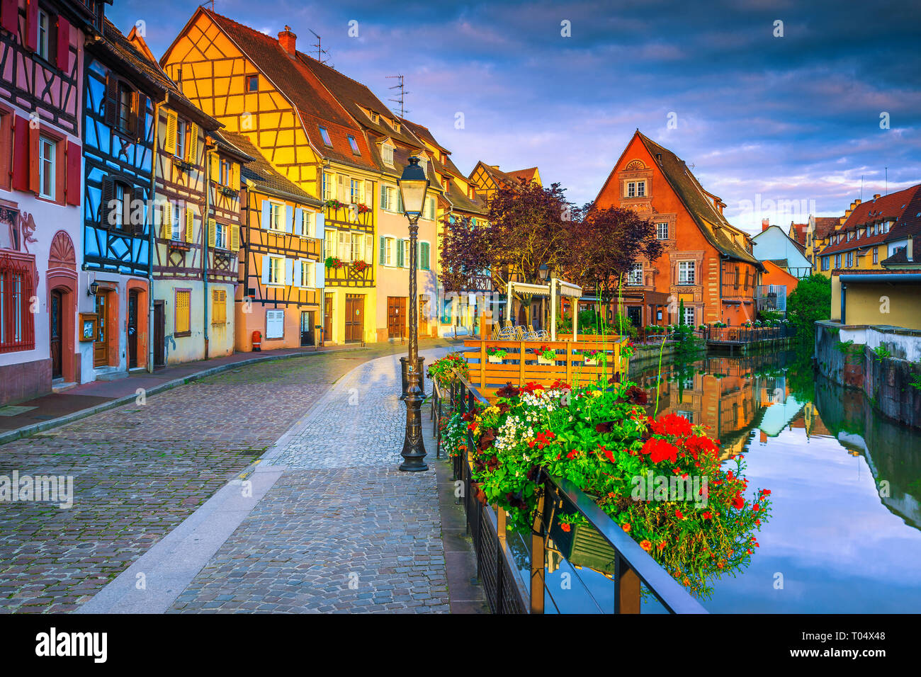 Famous summer travel destination, stunning colorful traditional houses and paved touristic street decorated with flowers at sunrise, Colmar, France, E Stock Photo