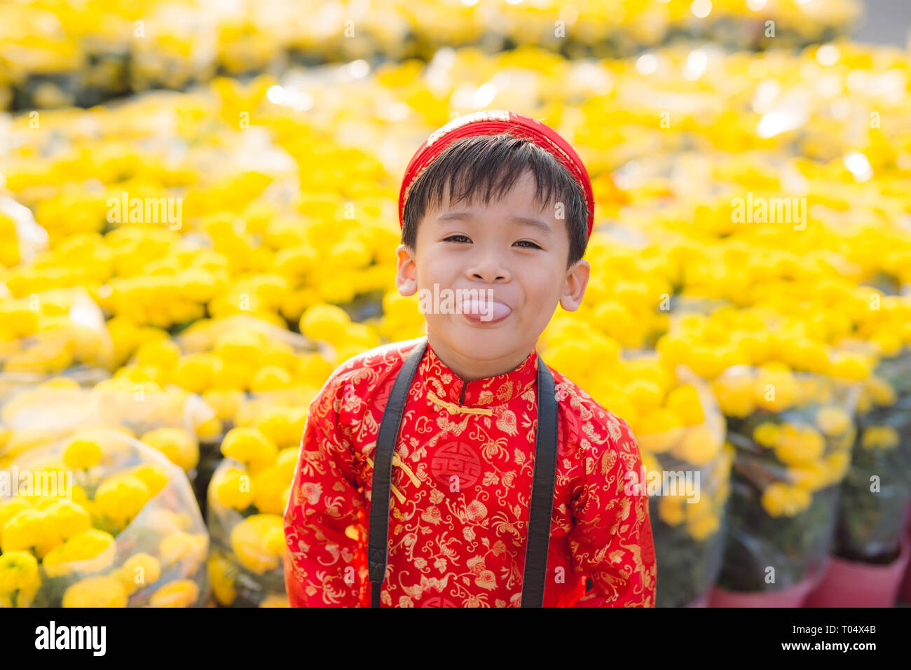 Having fun asian kid at marigold garden. Portrait of funny kid wearing Vietnamese traditional dress (Ao Dai) at Tet holiday Stock Photo