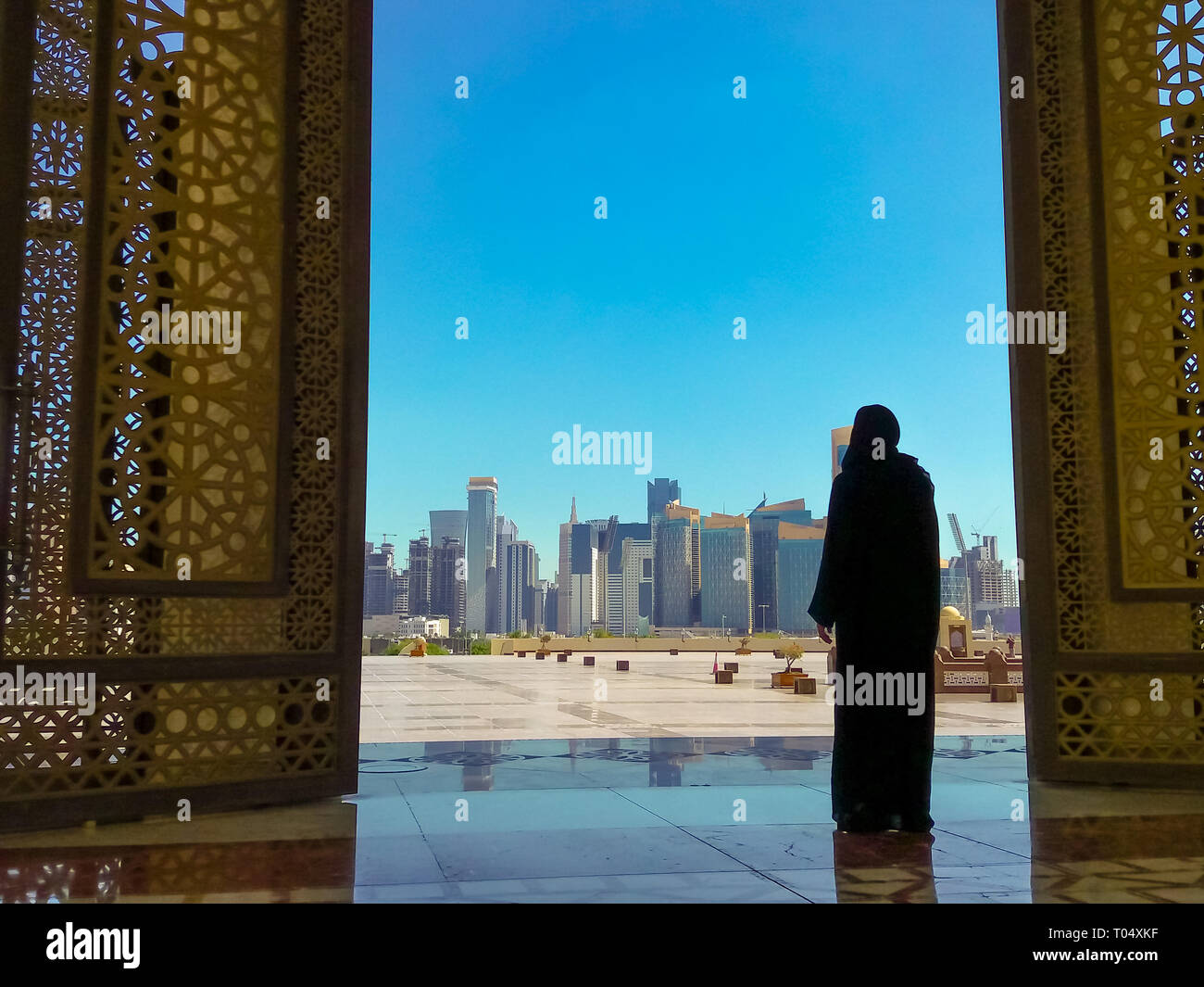 Woman with abaya dress looks at views of modern skyscrapers of Doha West Bay skyline outdoors State Grand Mosque in Doha, Qatar, Middle East, Arabian Stock Photo