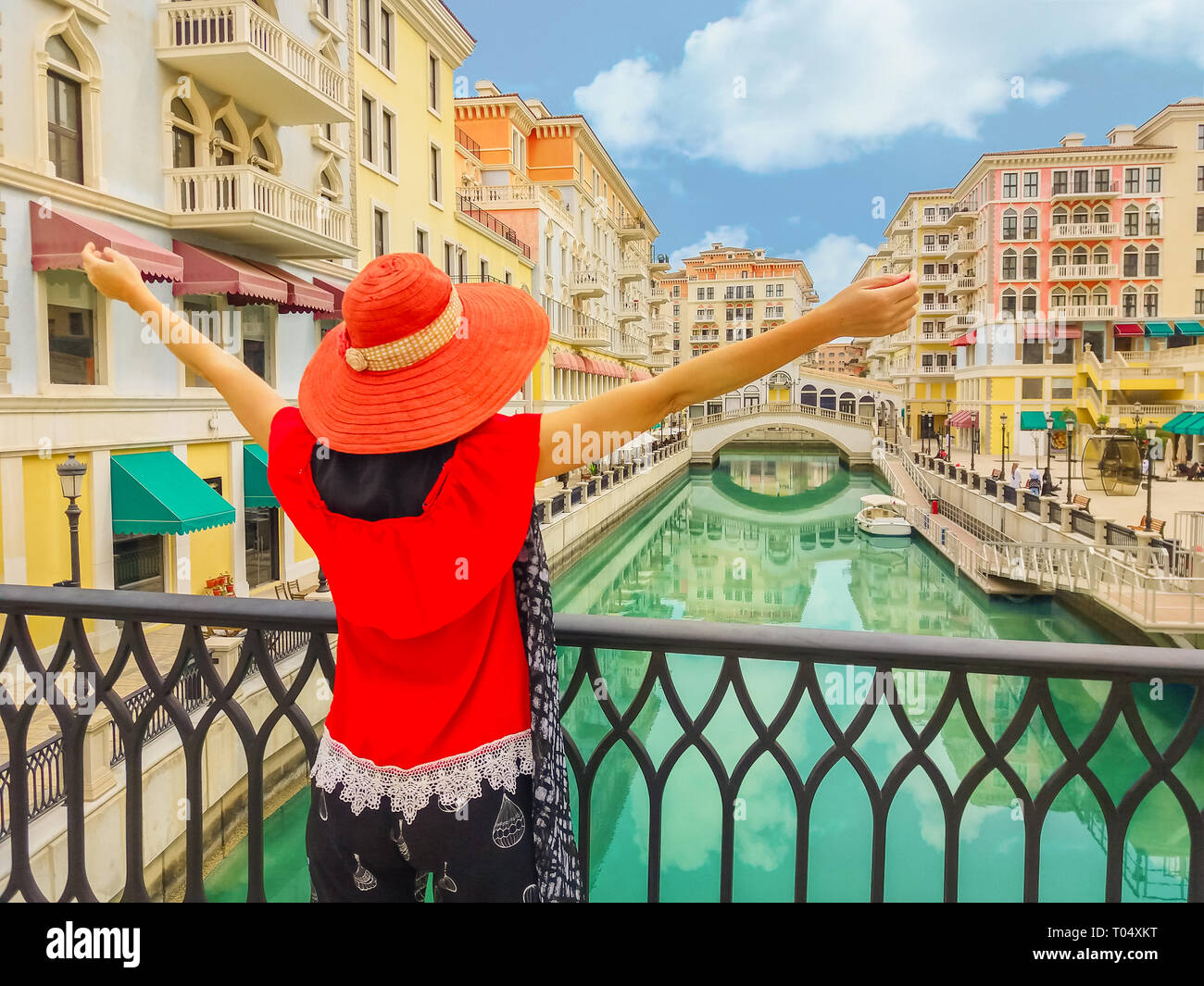 Tourism in Qatar. Woman with open arms on balcony at famous bridge reflecting on waters of canals in Venice Doha city. Caucasian tourist at Qanat Stock Photo