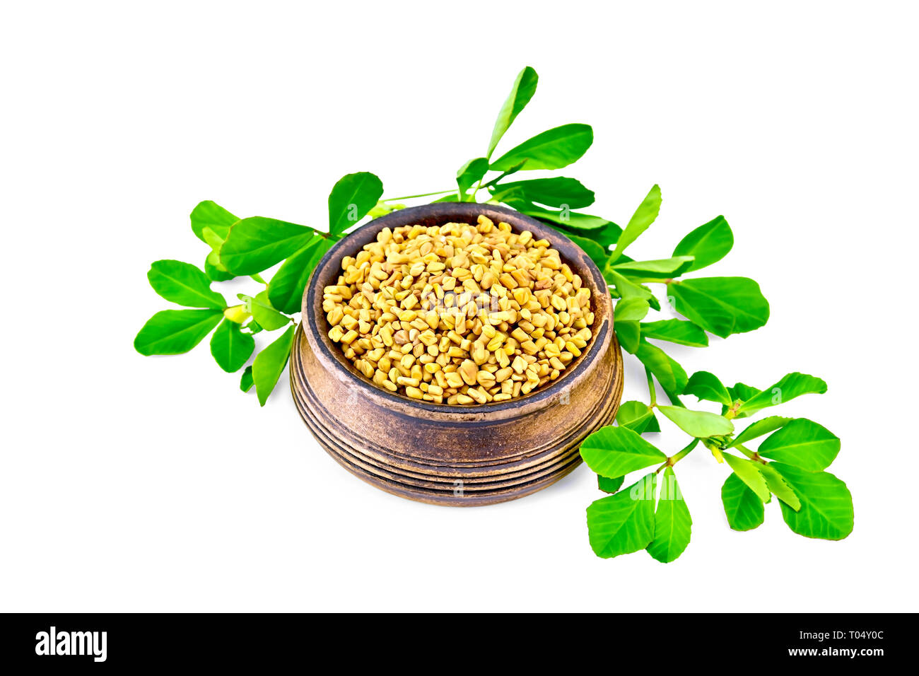 Fenugreek seeds in a small bowl with green leaves isolated on white background Stock Photo