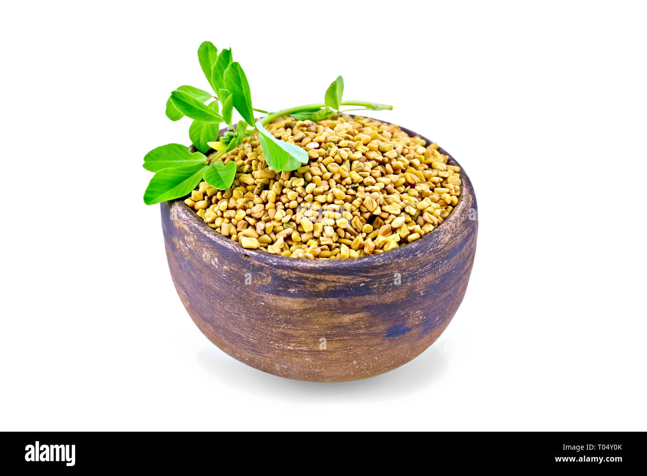 Fenugreek seeds in a clay bowl with green leaves isolated on white background Stock Photo