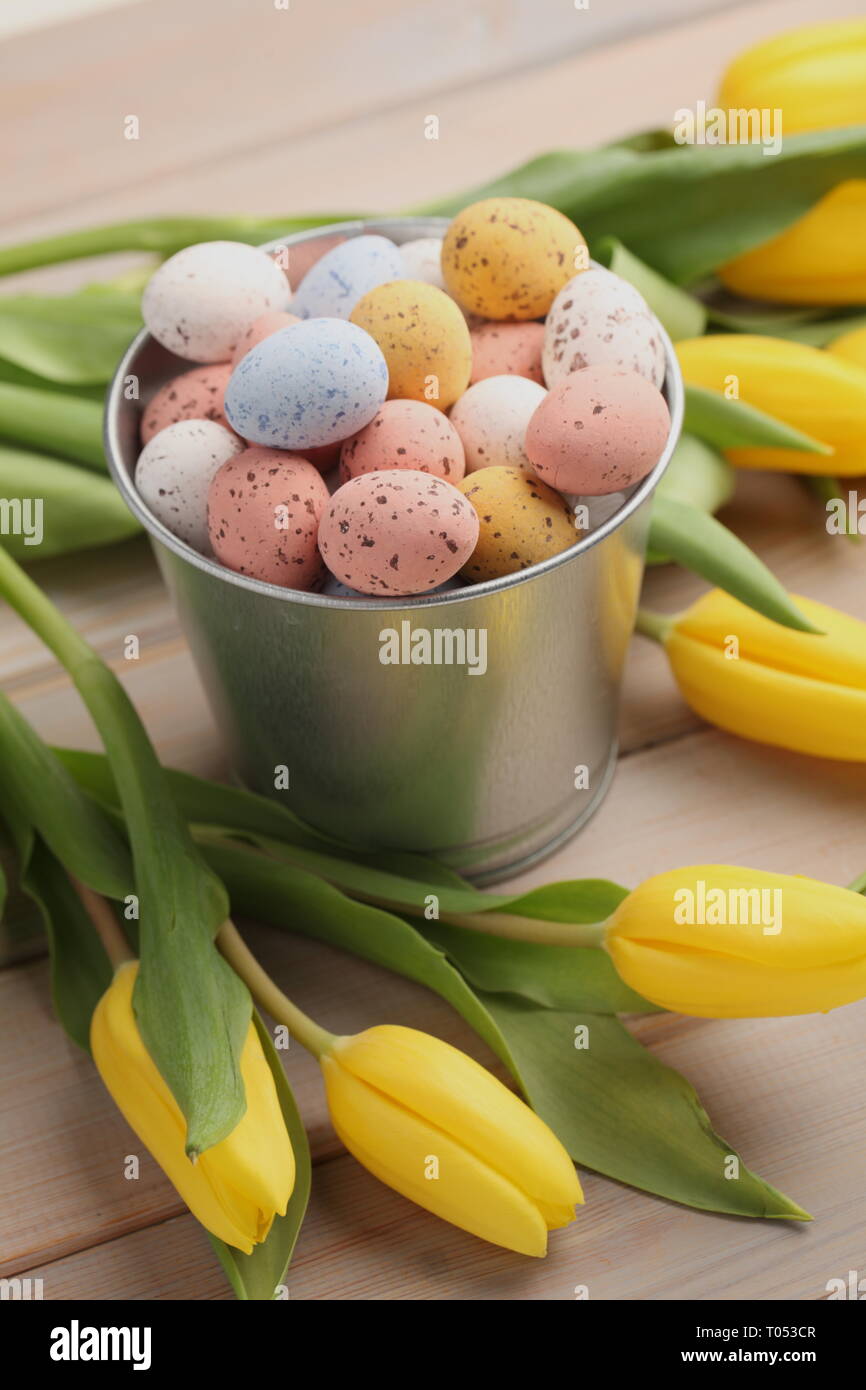 Colorful easter candy eggs with yellow tulips on wooden table Stock Photo
