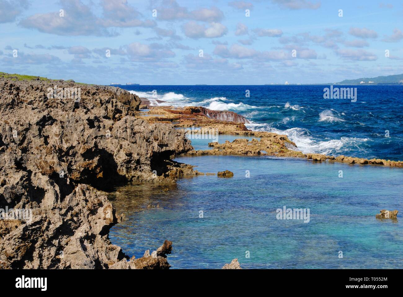 Sharp rocky shorelines with clear blue waters of the Tinian channel and a view of Saipan island in the far distance Stock Photo