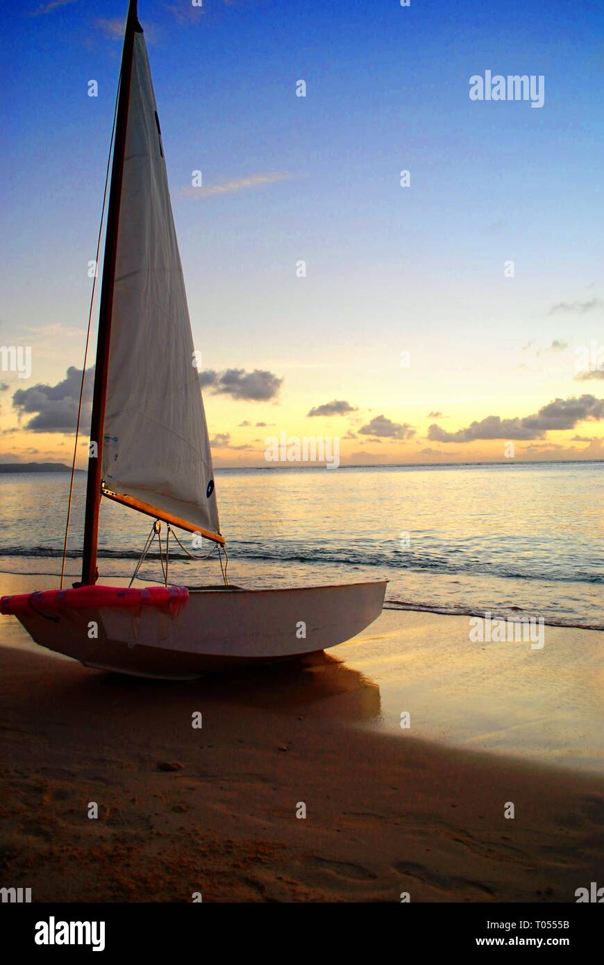 Sailboat docked on the shores of a beach at sunset Stock Photo