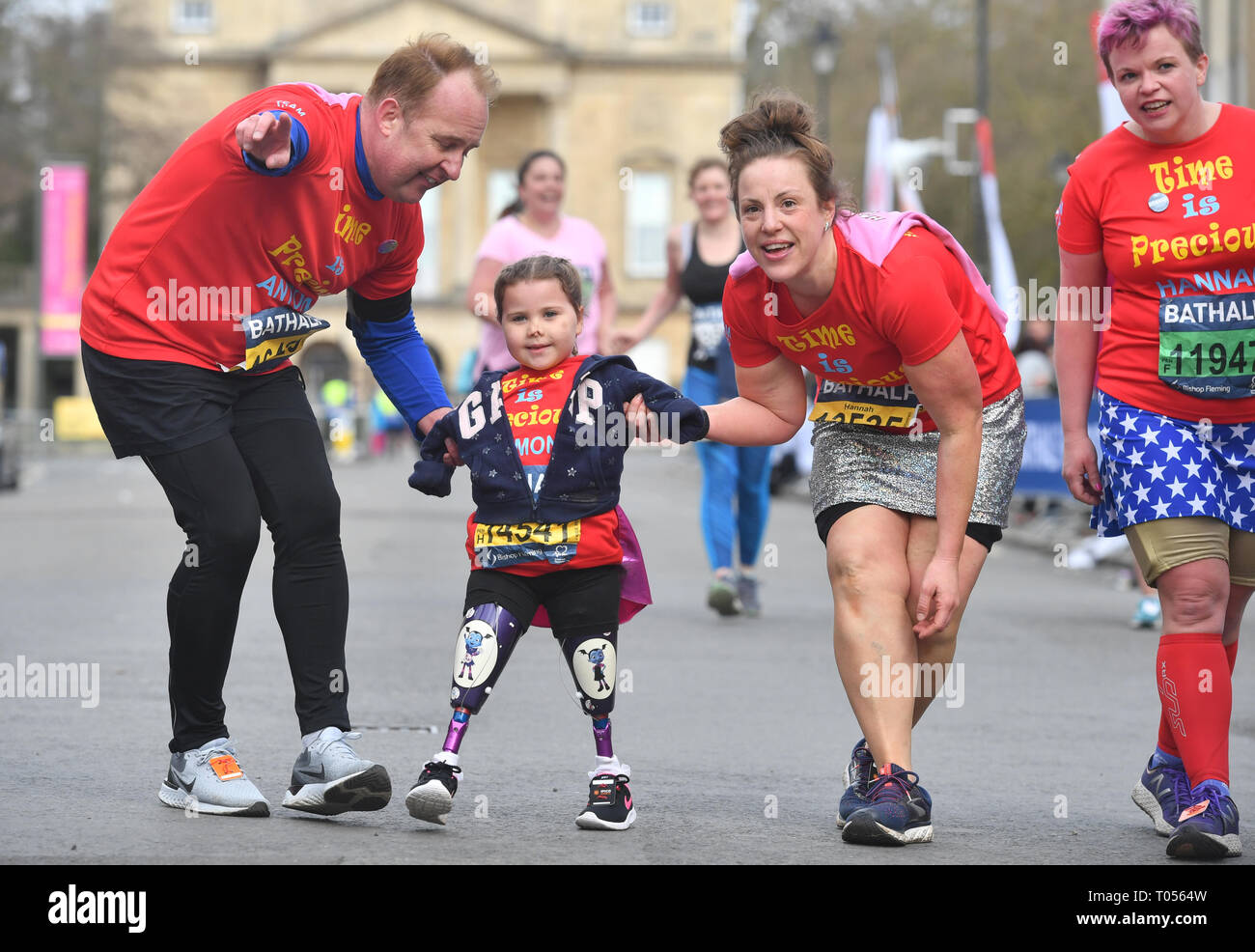 Five-year-old Harmonie-Rose Allen, who lost her limbs to meningitis, crossing the finishing line in the Bath Half Marathon with the help of her teacher Antony Wainer and her auntie Hannah Hall. Stock Photo