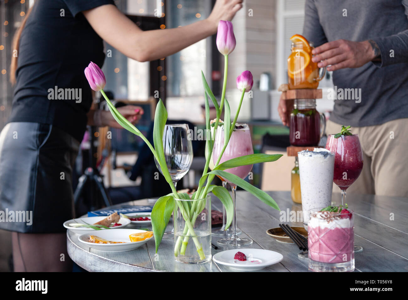 Food stylist and photographer decorate, preparing to shoot various cocktails, milkshakes, smoothies, flower tulips in vase on table. Concept professio Stock Photo
