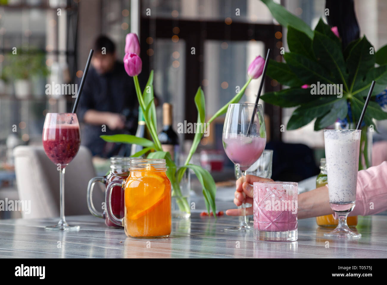 Food stylist and photographer decorate, preparing to shoot various cocktails, milkshakes, smoothies, flower tulips in vase on table. Concept professio Stock Photo