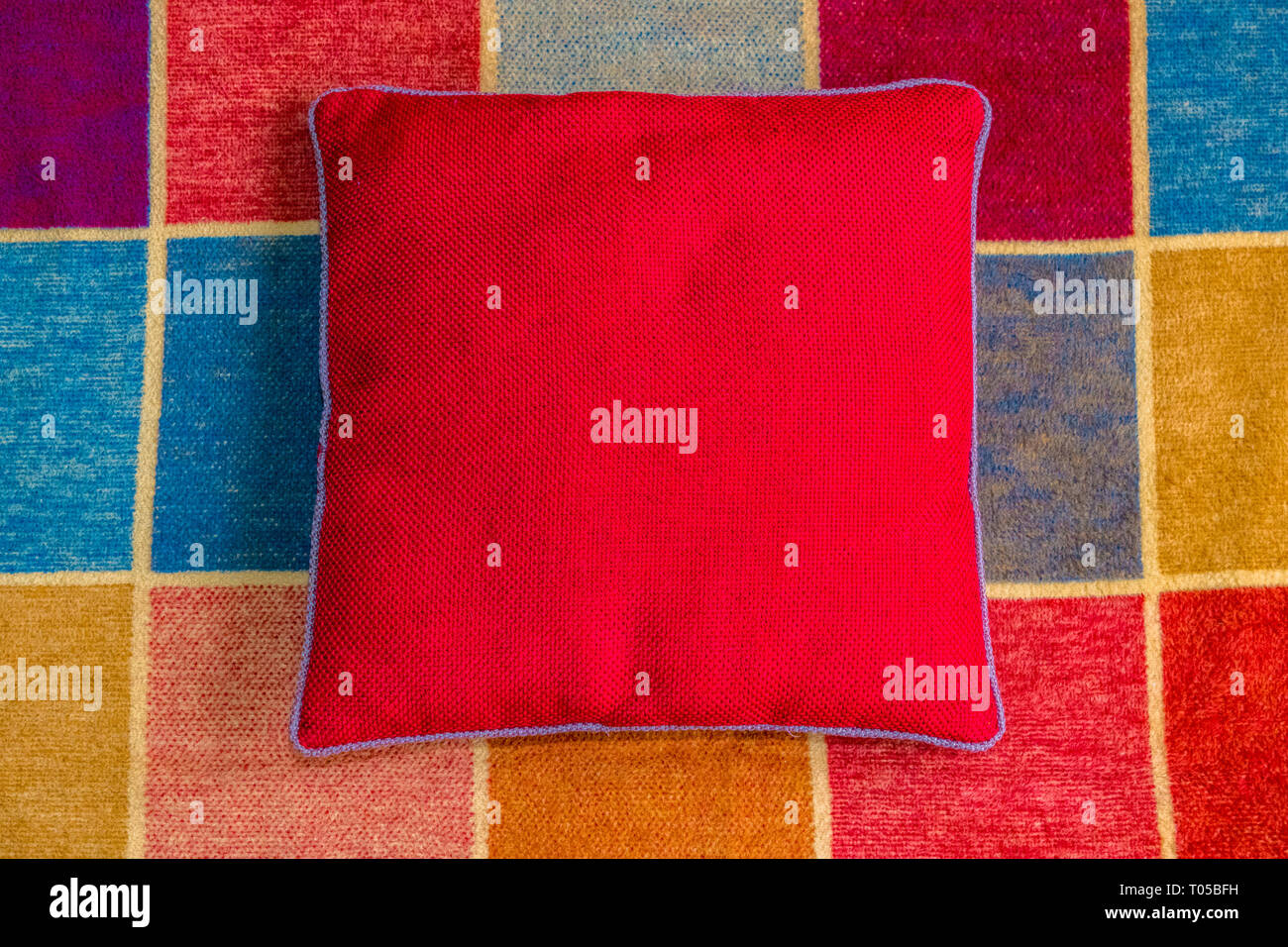 Red covered cushion on a multi coloured squared rug Stock Photo Alamy