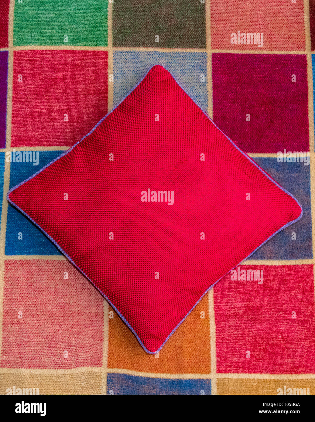 Red covered cushion on a multi coloured squared rug Stock Photo Alamy