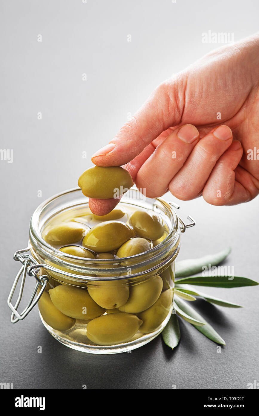 Pickled green olives in glass jar close up. Eating with hands Stock