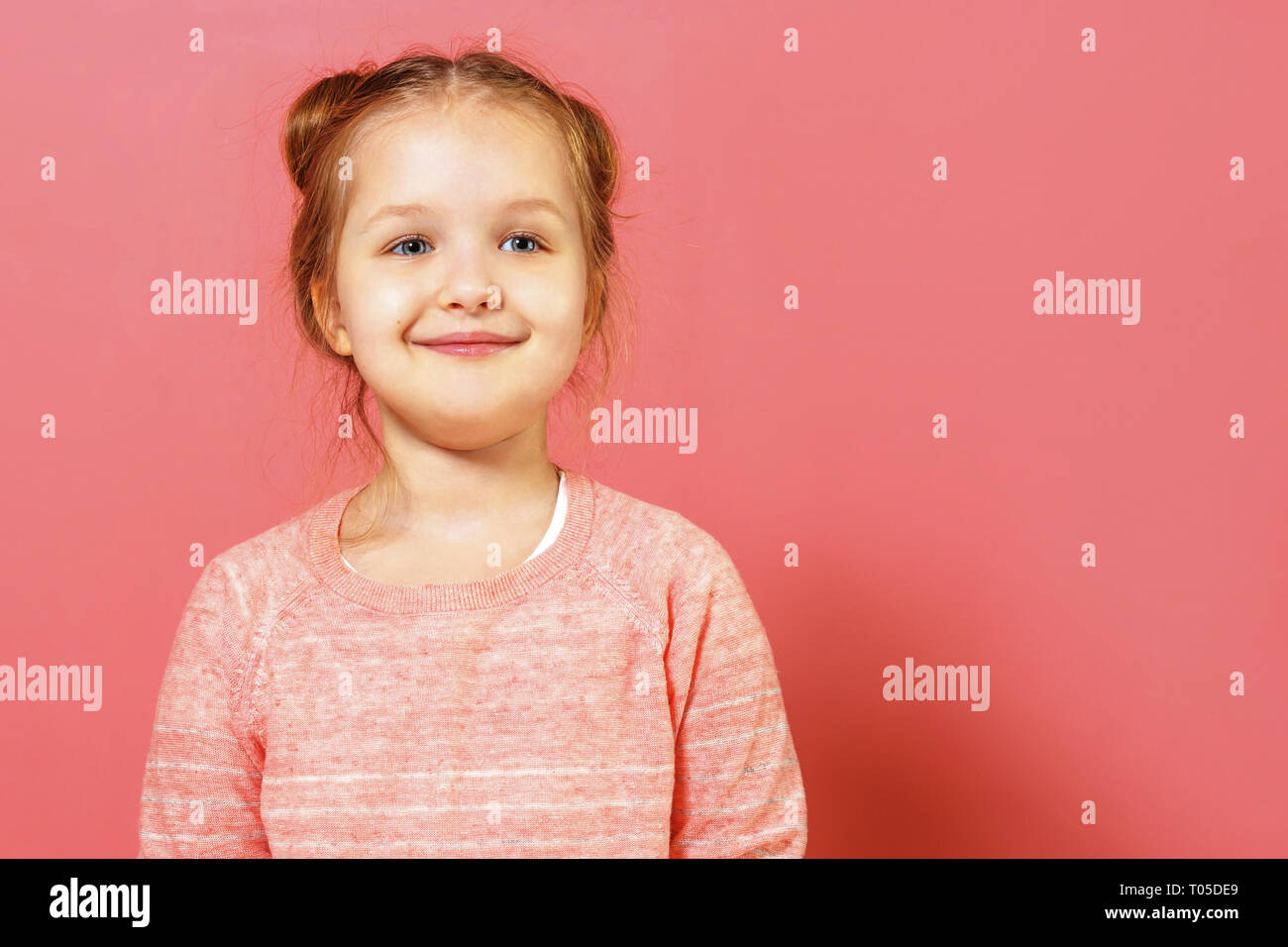 Closeup portrait of cute little child girl with buns of hair over pink background Stock Photo
