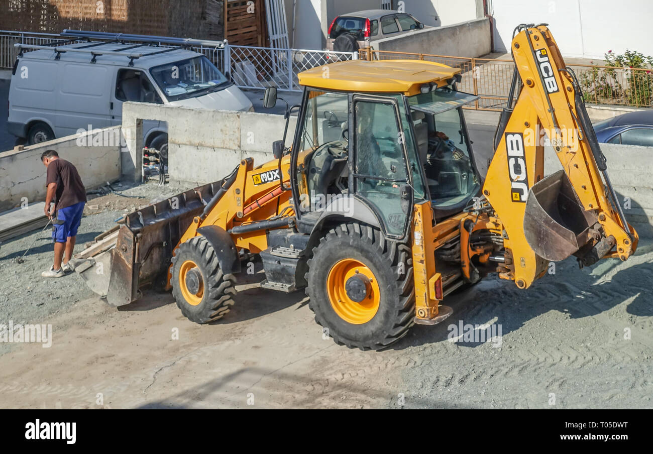 Limassol, Cyprus - November 4, 2018: Large yellow JCB tractor on a building site. Vehicle is large in the frame.  Man with tape measure in front of th Stock Photo