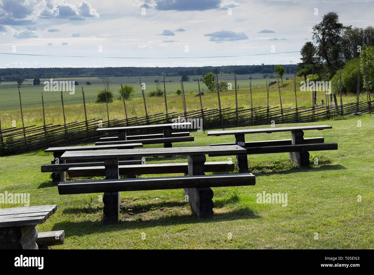 Guest resting area benches at the Linnaeus Hammarby Estate museum site surrounded by traditional Swedish roundpoles wooden fencing. Uppsala, Sweden. Stock Photo