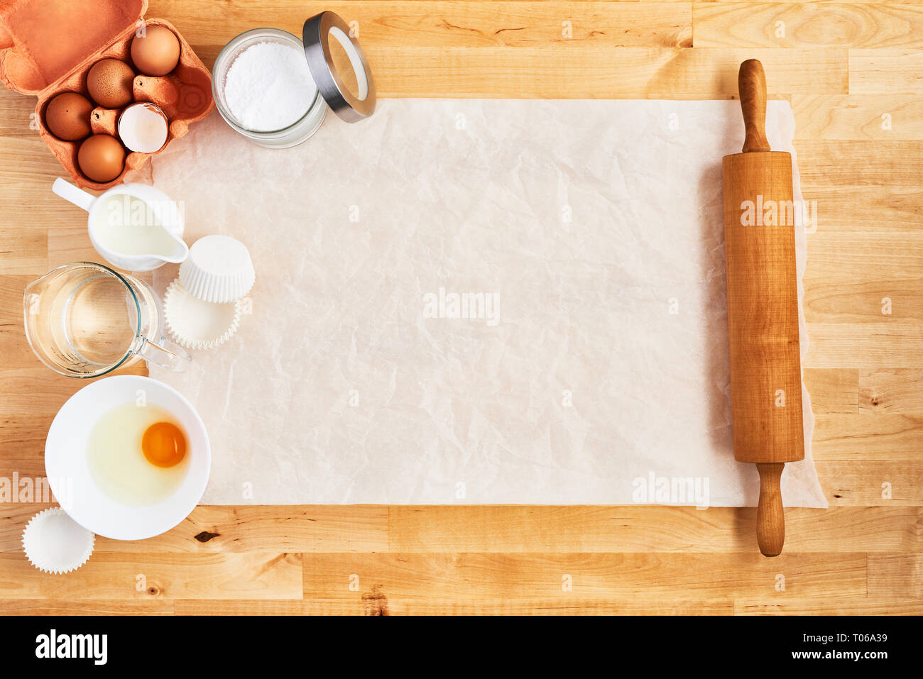 Rolling pin, food ingredients and kitchen utensils on crumpled piece of white parchment or baking paper on wooden table. Baking background concept. To Stock Photo