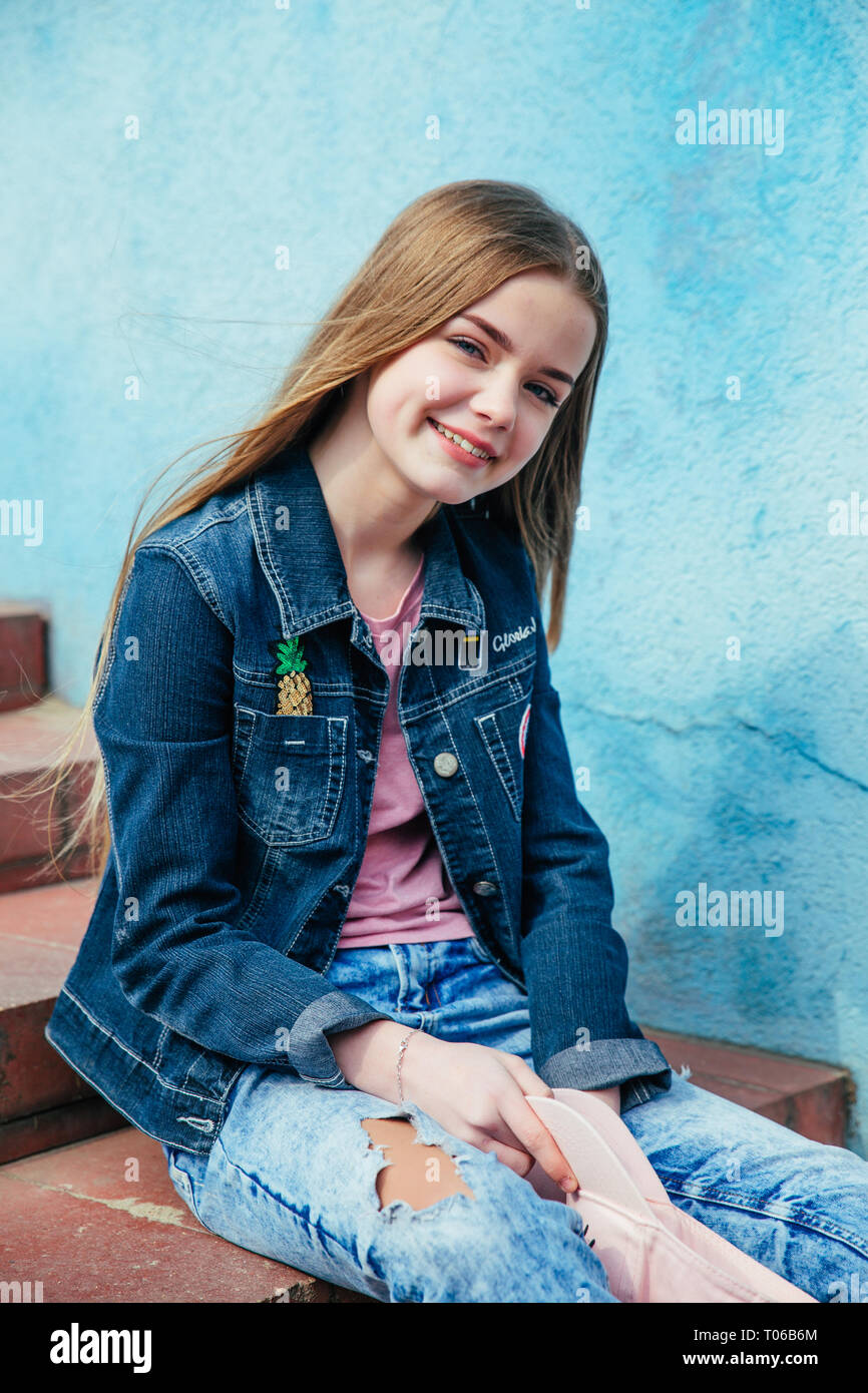 Portrait closeup beautiful smiling teenager girl in hat and denim jacket over blue wall Stock Photo