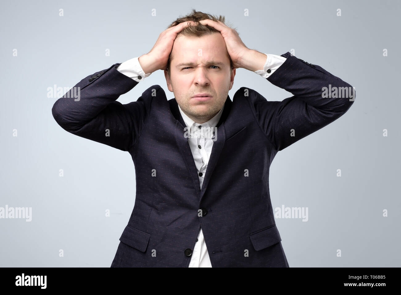 Doubtful handsome man in suit standing touching his head and looking at caemra, thinking. Stock Photo