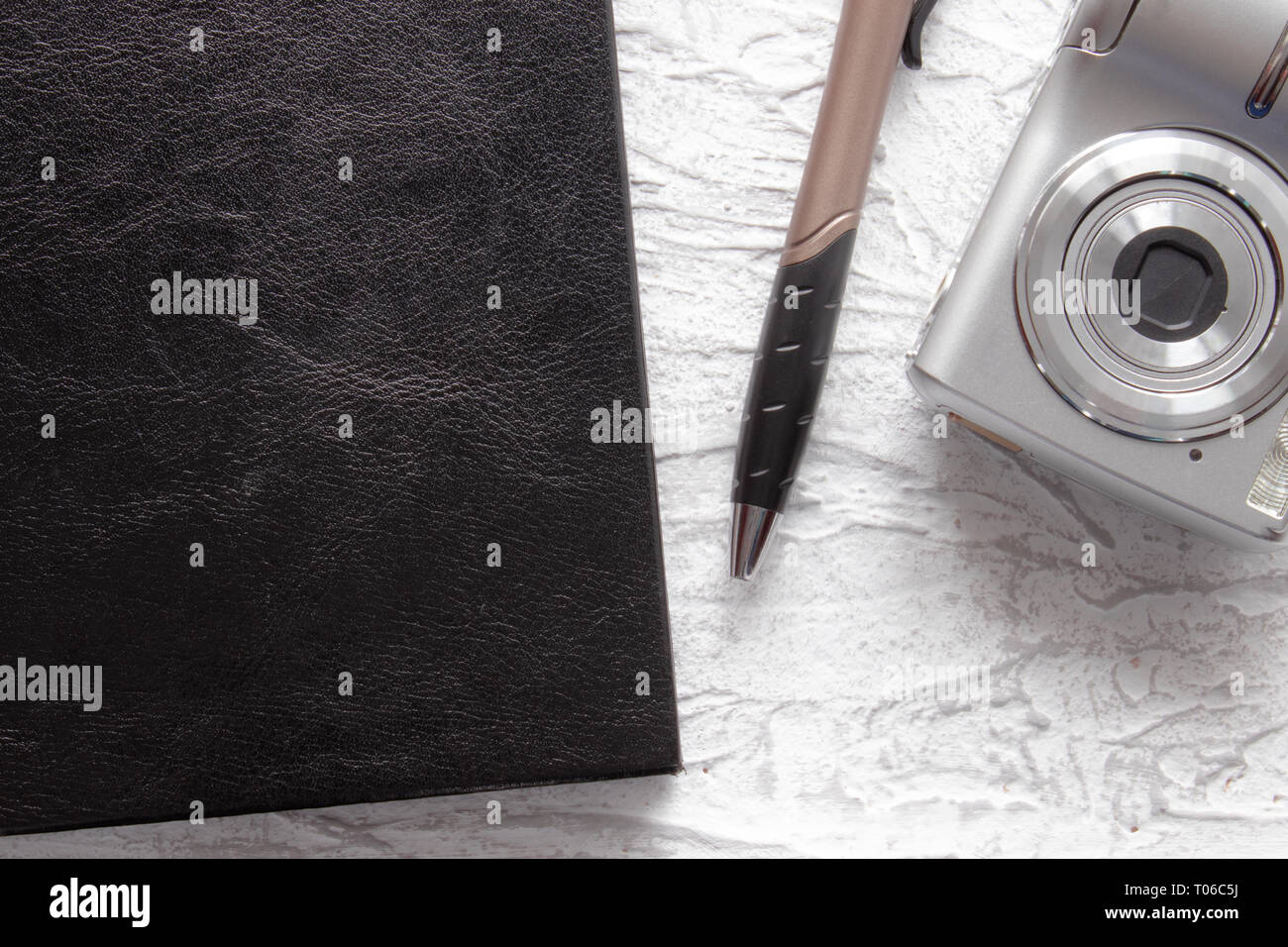 Top view of black notebook and pen near photo camera on white desk ...