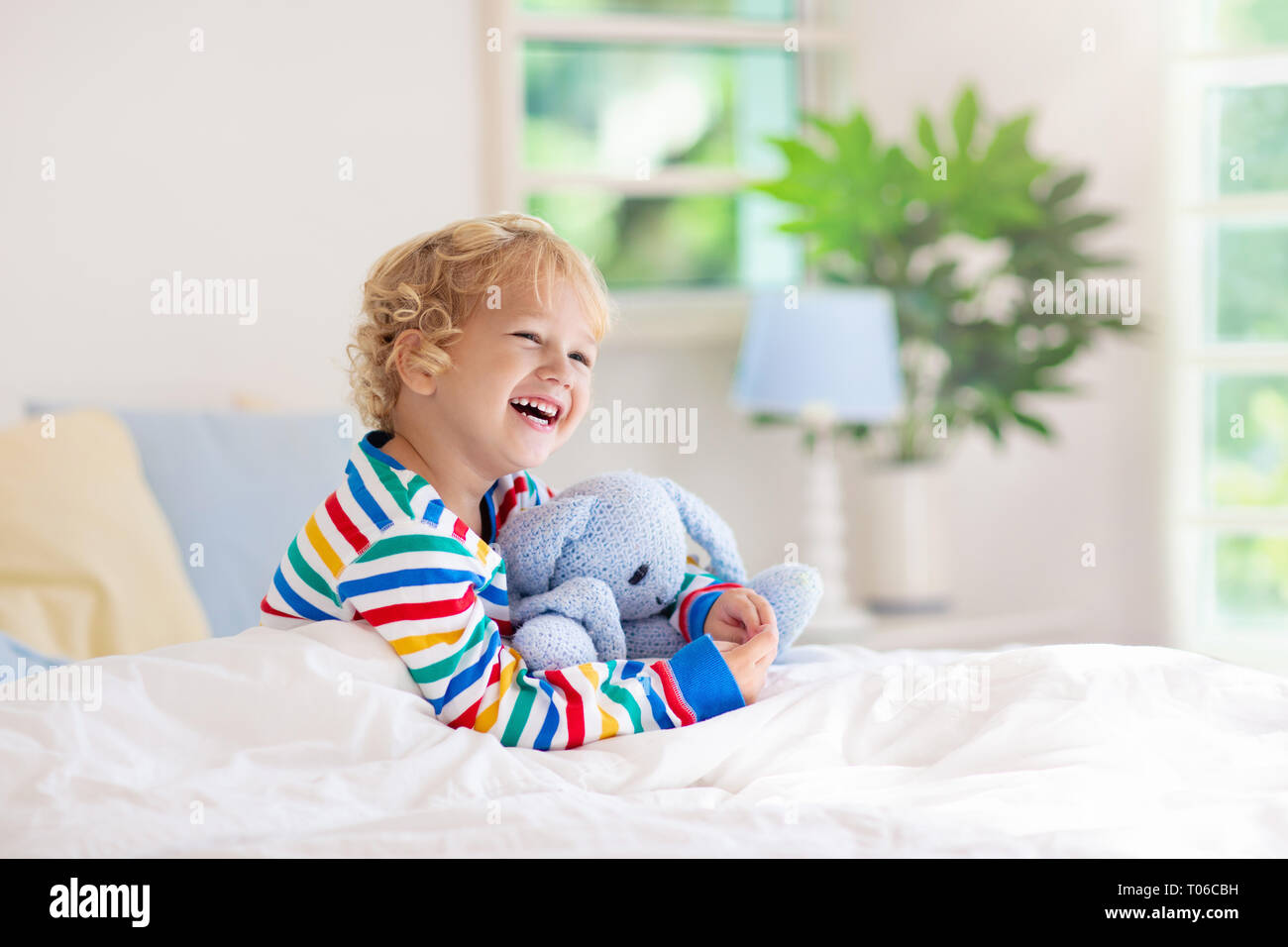 Child playing in bed in white sunny bedroom with window. Kids room and