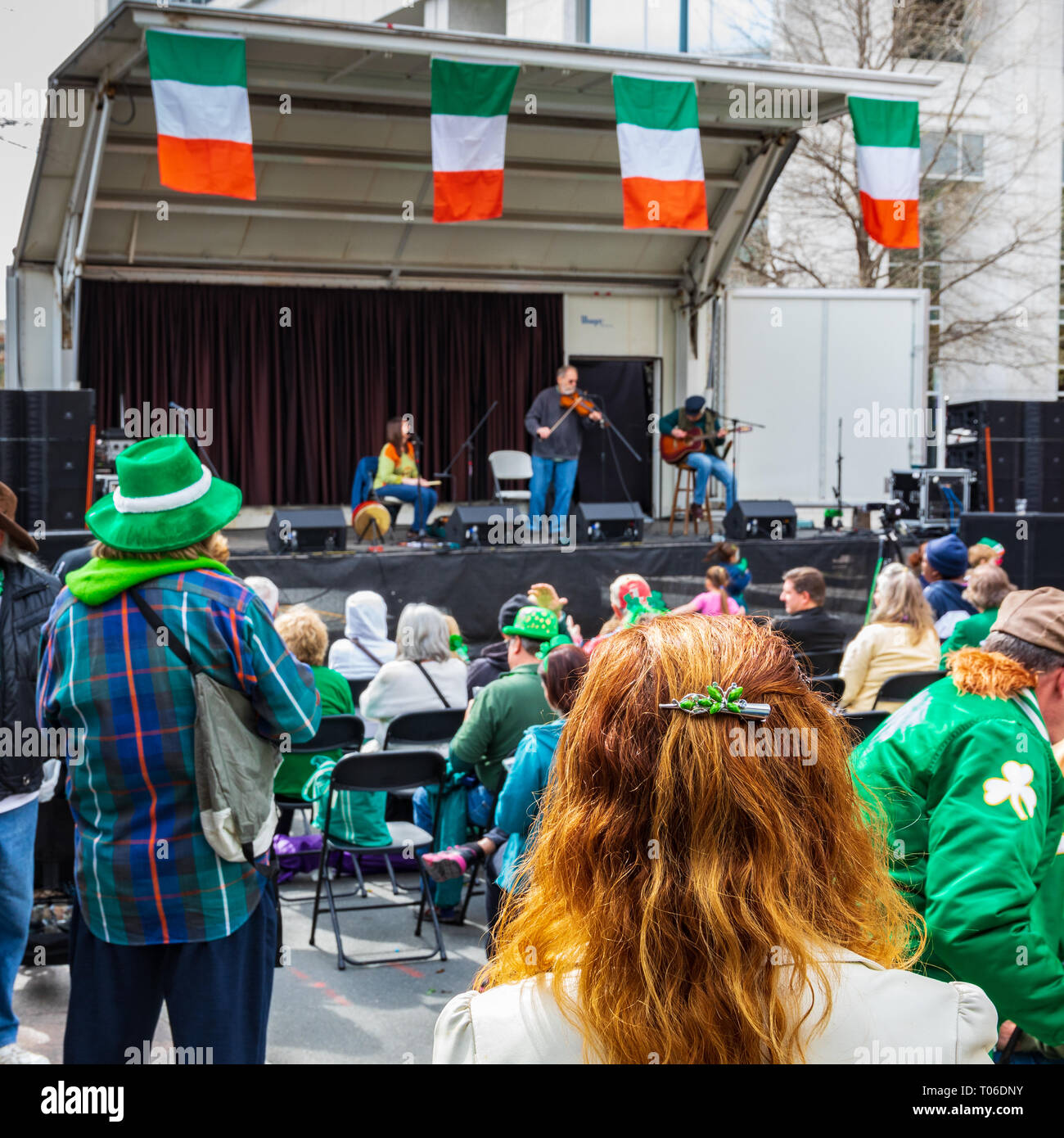 CHARLOTTE, NC, USA-3/16/19: A red-haired woman stands and listens to an Irish music band on St. Patrick's Day in uptown Charlotte. Stock Photo
