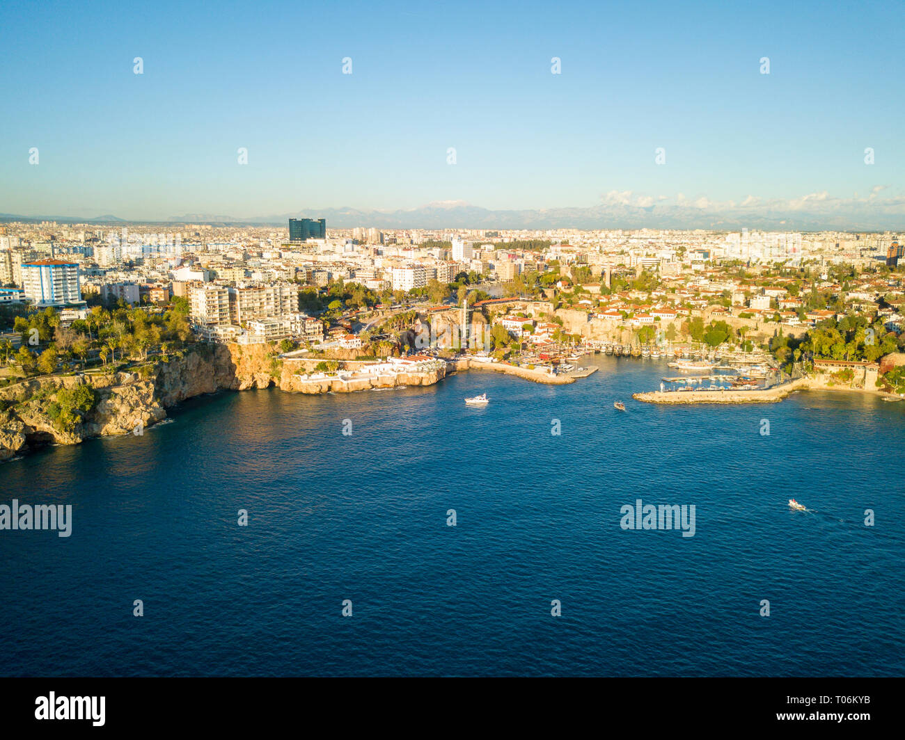 Aerial drone view of boats going into Kaleici old town harbor with cityscape and mountain background in Antalya, Turkey Stock Photo