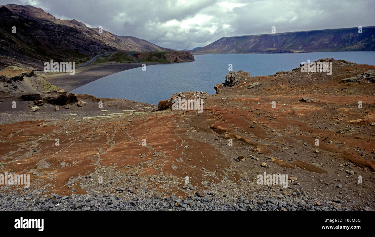 an Inland Lake and coastline roads in the volcanic landscape of central Iceland. A barren rugged lake shore is filled with volcanic rocks. Stock Photo