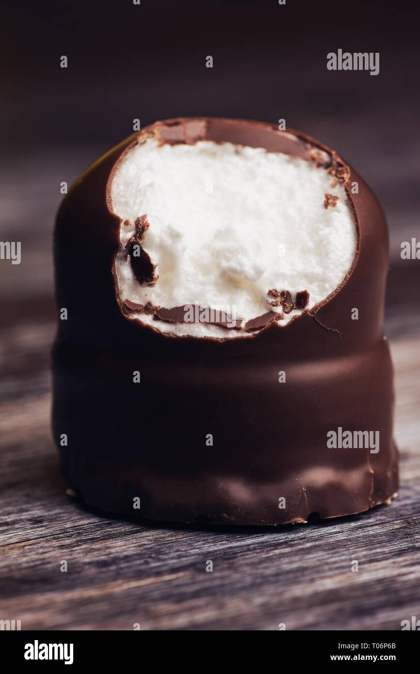 chocolate covered marshmallow, one part bitten off on brown wooden surface Stock Photo