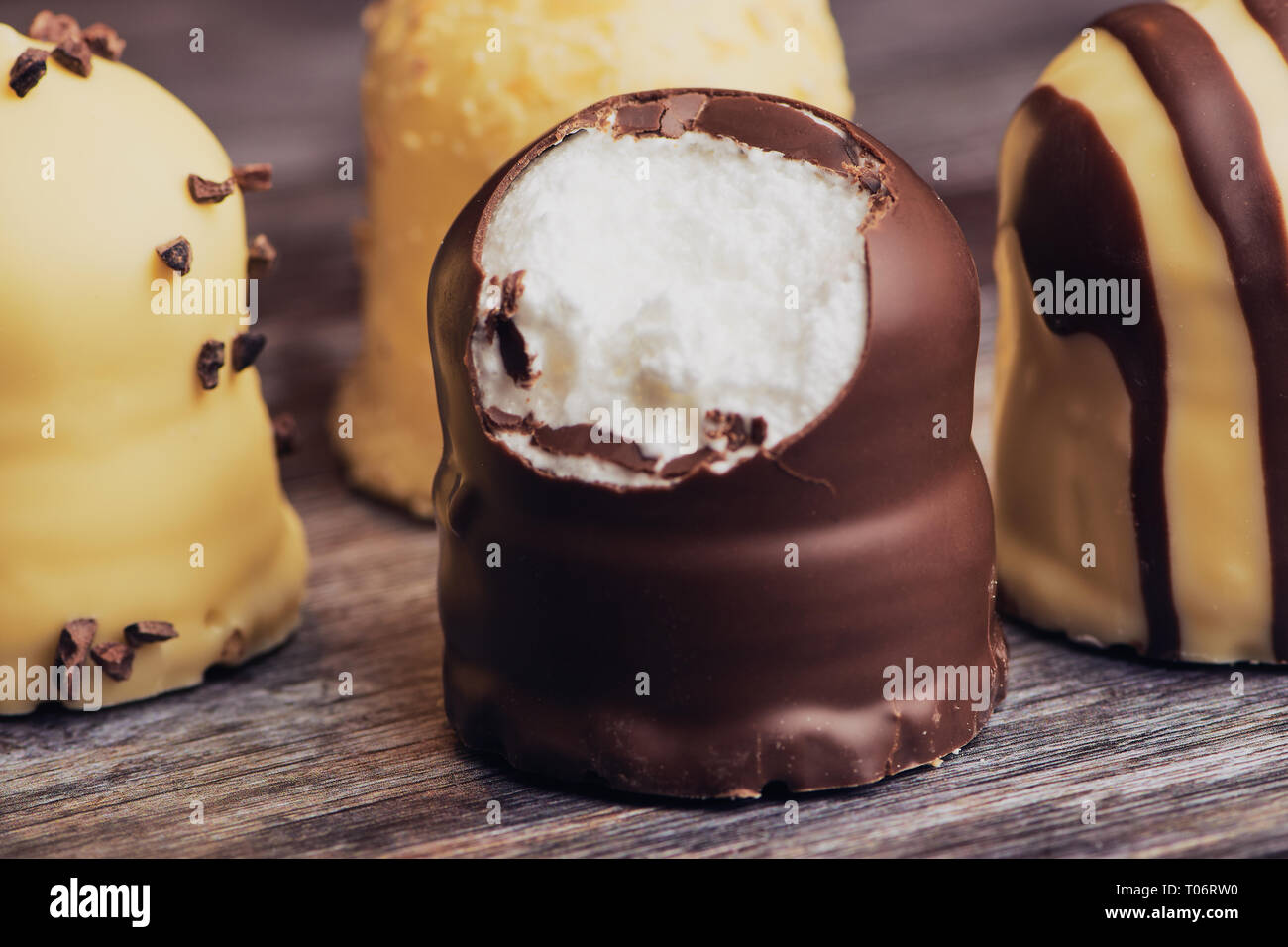 group of white and dark chocolate covered marshmallows. one is bitten off, on a brown wooden background Stock Photo