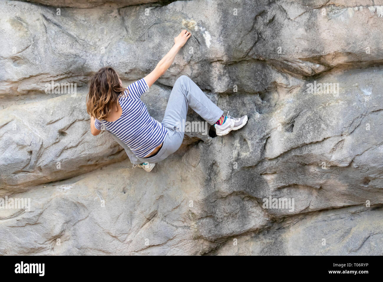 Young woman with long hair hanging on a rocky face of a mountain while climbing up without a rope support Stock Photo