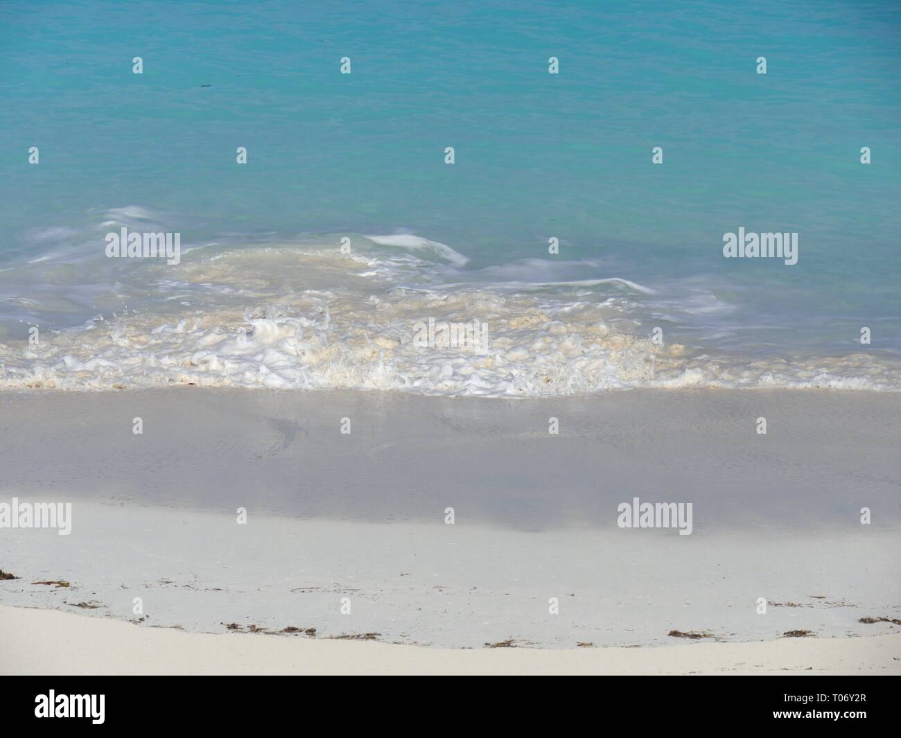 Waves rolling gently against the soft white sand create stunning patterns of foam in a tropical beach Stock Photo